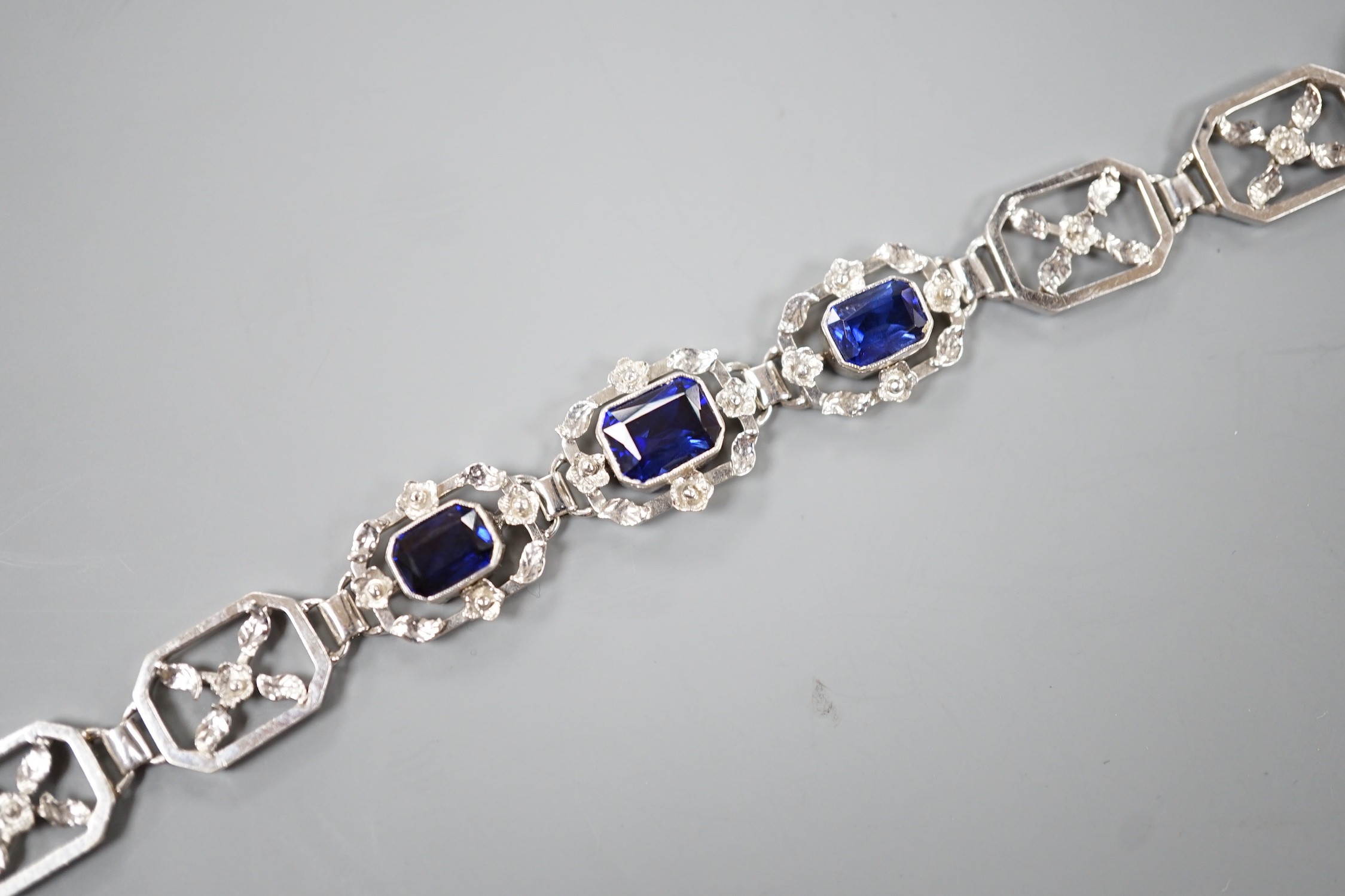 A modern 9ct white metal and three stone emerald cut synthetic sapphire set pierced link bracelet, approx. 18cm, gross weight 16.7 grams.